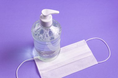 Açık mavi arka planda alkol jeli ve cerrahi maskeli konteynır.