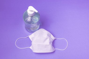 Açık mavi arka planda alkol jeli ve cerrahi maskeli konteynır.