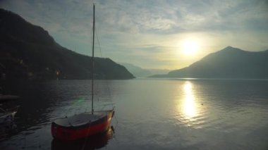 Günbatımından önce İtalya 'daki Como Gölü' nün kıyısına demir atmış bir yat alp tepelerinin dağ ufkunda. Sinematik çerçeve. Romantik atmosfer. Sakin ve huzur verici bir sahne. Yelkenli.