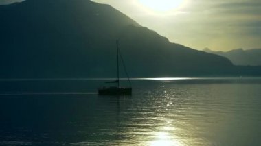 Günbatımından önce İtalya 'daki Como Gölü' nün kıyısına demir atmış bir yat alp tepelerinin dağ ufkunda. Sinematik çerçeve. Romantik atmosfer. Sakin ve huzur verici bir sahne. Yelkenli.