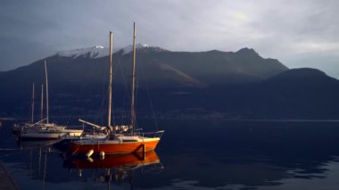 Günbatımından önce İtalya 'daki Como Gölü' nün kıyısına demir atmış bir yat alp tepelerinin dağ ufkunda. Sinematik çerçeve. Romantik atmosfer. Sakin ve huzur verici bir sahne. Yelkenli.