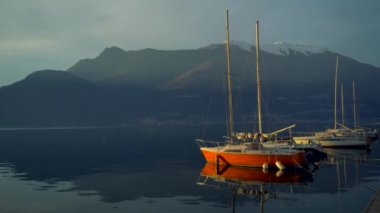 Günbatımından önce İtalya 'daki Como Gölü' nün kıyısına demir atmış bir yat alp tepelerinin dağ ufkunda. Sinematik çerçeve. Romantik atmosfer. Sakin ve huzur verici bir sahne. Yelkenli.