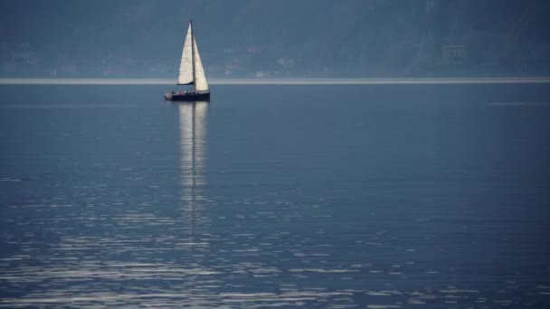 イタリアのコモ湖 日没時に帆船で旅行する 映画のパノラマ 緑の山々を背景にボード上の愛好家と豪華なセーリングヨット遠征 ロマンチックな旅 白い帆 — ストック動画