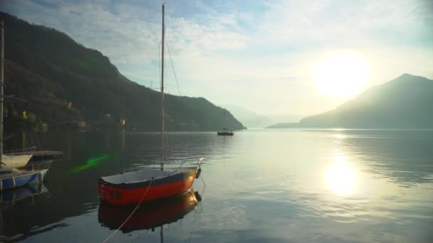 Plachetnice kotvící u pobřeží jezera Como v Itálii před západem slunce nad horským obzorem vysokohorských štítů. Filmový snímek. Romantická atmosféra. Klidná a uklidňující scéna. Plachetnice