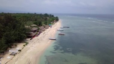 Gili Air, Endonezya: İnsansız hava aracı ile bir adanın vurulması. Adanın çerçevesinde, sahil bölgesinde, kıyıya demir atmış nakliye gemileri. Panoramik görüntüler. Bulutlu hava. 