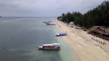Gili Air, Endonezya: İnsansız hava aracı ile bir adanın vurulması. Adanın çerçevesinde, sahil bölgesinde, kıyıya demir atmış nakliye gemileri. Panoramik görüntüler. Bulutlu hava. 