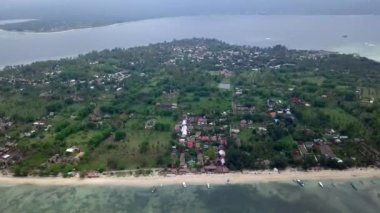 Gili Air, Endonezya: İnsansız hava aracı ile bir adanın vurulması. Adanın çerçevesinde, sahil bölgesinde, kıyıya demir atmış nakliye gemileri. Panoramik görüntüler. Bulutlu hava. 