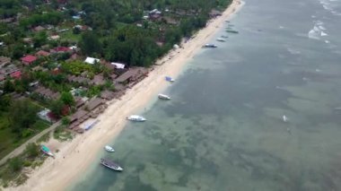 Gili Air, Endonezya: İnsansız hava aracı ile bir adanın vurulması. Adanın çerçevesinde, sahil bölgesinde, kıyıya demir atmış nakliye gemileri. Panoramik görüntüler. Bulutlu hava. 