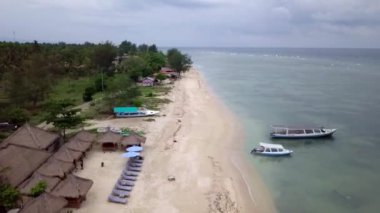 Gili Air, Endonezya: İnsansız hava aracı ile bir adanın vurulması. Adanın çerçevesinde, sahil bölgesinde, kıyıya demir atmış nakliye gemileri. Panoramik görüntüler. Bulutlu hava. 