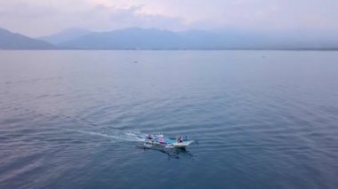 Gili Air, Endonezya: İnsansız hava aracı ile bir adanın vurulması. Adanın çerçevesinde, sahil bölgesinde, kıyıya demir atmış nakliye gemileri. Panoramik görüntüler. Bulutlu hava. 