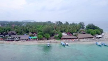Gili Air, Endonezya: İnsansız hava aracı ile bir adanın vurulması. Adanın çerçevesinde, sahil bölgesinde, kıyıya demir atmış nakliye gemileri. Panoramik görüntüler. Bulutlu hava. 