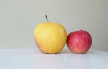 Büyük ve küçük kırmızı elmalar beyaz ahşap masada izole edilmiş.