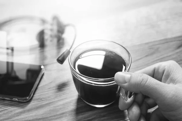 Mano sosteniendo taza de café o té y auriculares voip, teléfono inteligente en w —  Fotos de Stock