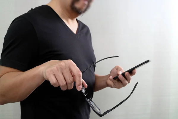 Designer χέρι εκμετάλλευση γυαλιά, χρησιμοποιώντας έξυπνο τηλέφωνο στο λευκό πίσω — Φωτογραφία Αρχείου