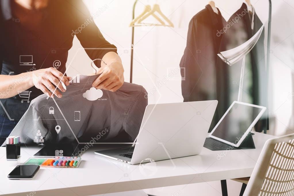 Fashion designer holding shirt and using laptop with digital tab