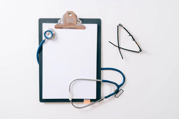 Stethoskop und graues Klemmbrett und Brille auf weißem Grund — Stockfoto