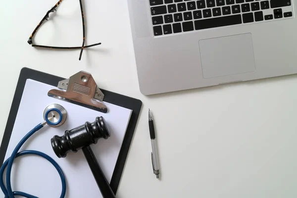 Gavel escuro com estetoscópio médico perto do portátil na mesa branca em — Fotografia de Stock