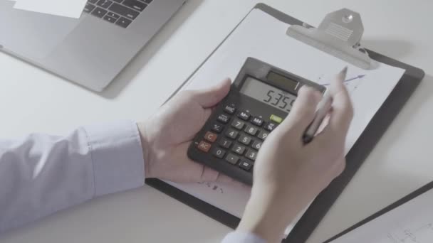 現代のオフィスの机の上に携帯電話でコストや計算機やラップトップについての財政とビジネスマンの手作業 — ストック動画