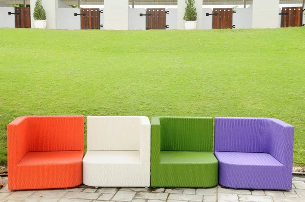 五颜六色的人工藤沙发在绿色围场旁边 — 图库照片