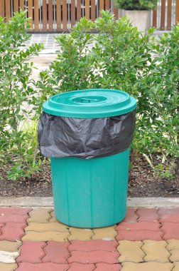 Plastik yeşil kova ile tuğla üzerinde siyah çöp torbası.