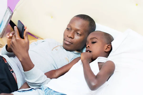 Otec a syn konzultuje mobilní telefon v posteli — Stock fotografie