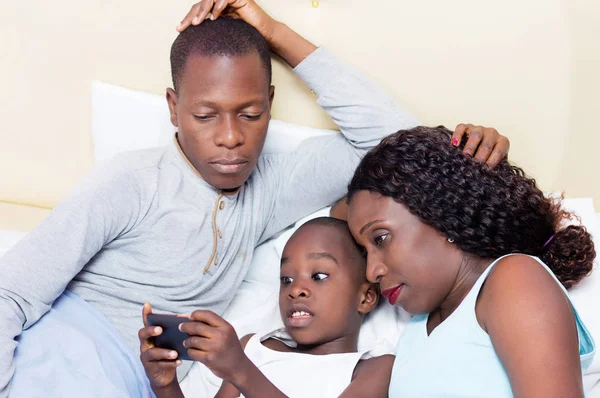 Mladá rodina sdílení mobilní telefon v posteli — Stock fotografie