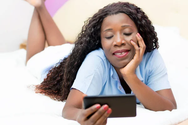 Smiling young woman using a mobile phone on her bed — Stock Photo, Image