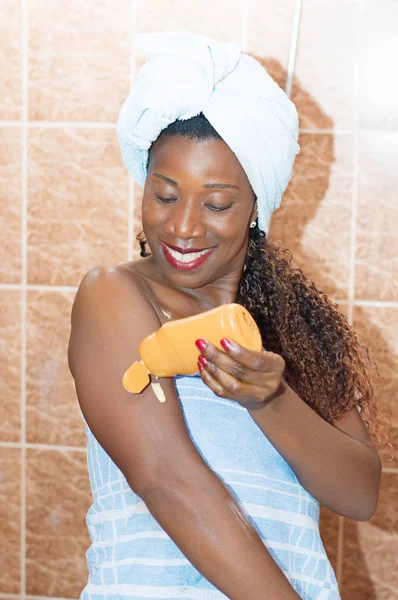 young woman applying body lotion after bath