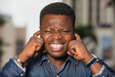 Sıkıcı gürültüyü görmezden gelerek kulaklarını kapatan yakışıklı genç adam.,