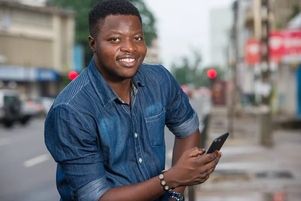 Homme souriant assis dehors et tenant son téléphone dans ses mains — Photo