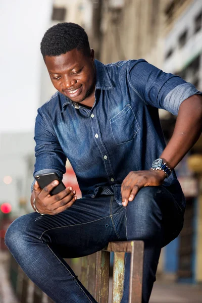 Portrait d'un jeune homme souriant assis avec un téléphone portable — Photo