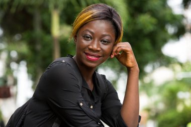 Gülümseyen öğrenci kız dışarıda oturuyor.