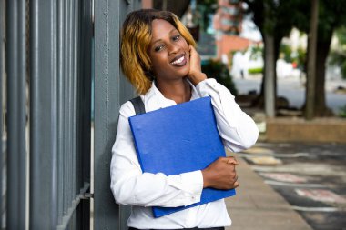 Dışarıda ayakta duran gülümseyen üniversite öğrencisinin portresi.