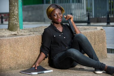 Genç kız dışarıda kampüste oturuyor ve ev ödevlerini yapıyor. Üniversite öğrencisi elinde kitabını tutuyor.