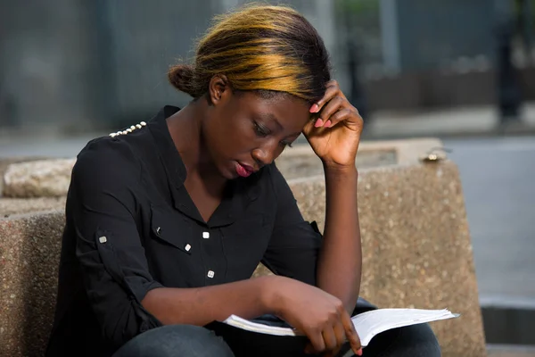 young student sitting in black shirt revising lessons with notebook on her thighs.