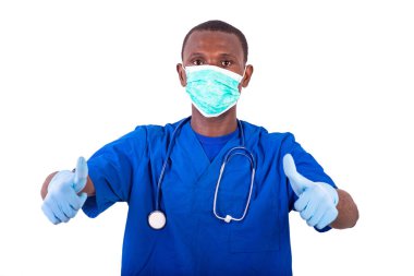 Genç doktor üniforma giyiyor, steteskop takıyor, tıbbi maske takıyor ve baş parmağını gösteriyor..