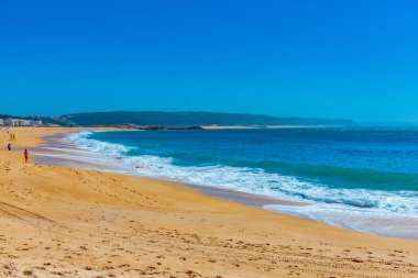 İnsanlar Portekiz 'de Nazare sahilinde güneşli bir günün tadını çıkarıyorlar.