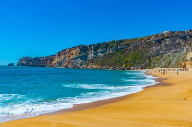 İnsanlar Portekiz 'de Nazare sahilinde güneşli bir günün tadını çıkarıyorlar.