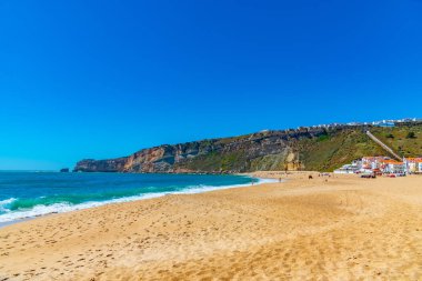 İnsanlar Portekiz 'de Nazare sahilinde güneşli bir günün tadını çıkarıyorlar.