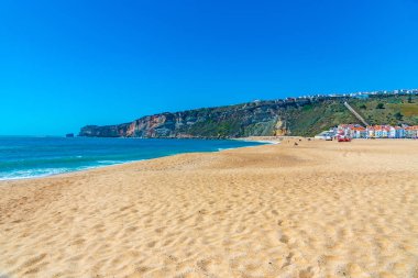 İnsanlar Portekiz 'de Nazare sahilinde güneşli bir günün tadını çıkarıyorlar.