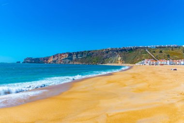 İnsanlar Portekiz 'de Nazare sahilinde güneşli bir günün tadını çıkarıyorlar.