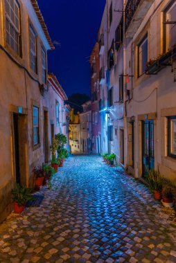 İnsanlar Alfama bölgesinde dar bir sokakta geziniyor. 