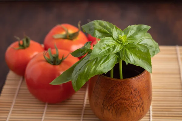 Ahşap kasede fesleğen yaprakları ahşap rafta ve arka planda domatesler var.