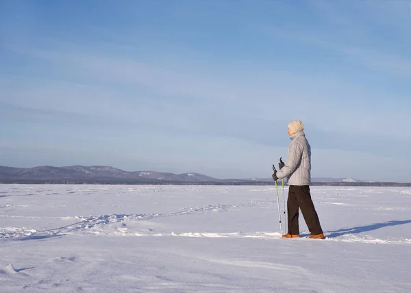 雪に覆われた湖、屋外、サイドビューで冬の晴れた日にノルディックウォーキングを単独で高齢者. — ストック写真