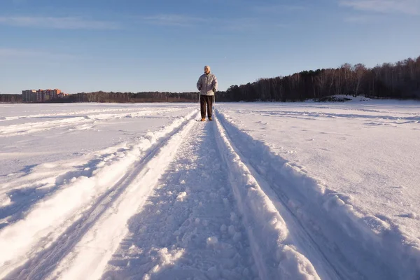 高齢者の女性は右のカメラで、広い角度をノルディック歩いて行く。冬の晴れた日の屋外、雪に覆われた湖. — ストック写真