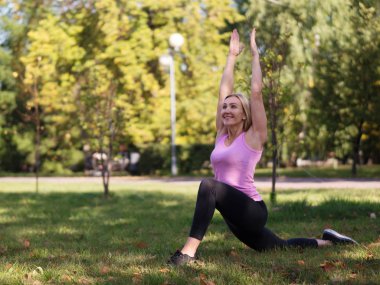 Caucasian smiling happy woman doing yoga on the grass outdoor in urban park, selective focus