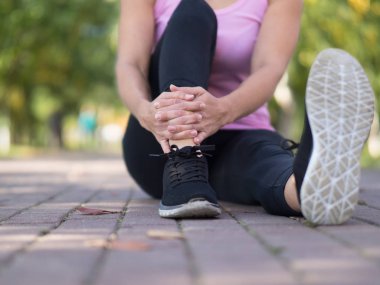 Headless body of caucasian woman in sports wear who sitting on the paved path in public park in summer and resting between exercises, close up. Urban work out outdoor, selective focus