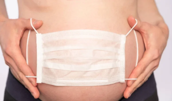 Беременная Женщина Держит Медицинскую Маску Брюшном Фоне — стоковое фото