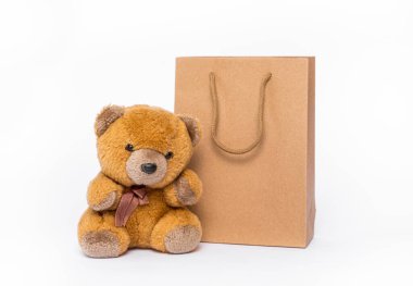 Teddy bear is near a craft paper packet; white background clipart