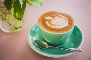 Yeşil fincanda güzel latte sanatıyla kahve ve kafedeki ahşap masada çay tabağı.